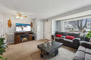 Carpeted living room with ceiling fan and a textured ceiling