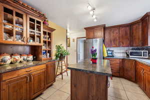 Kitchen with stainless steel refrigerator, a center island, light tile patterned floors, and decorative backsplash