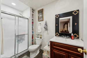 Bathroom featuring tile patterned flooring, toilet, a textured ceiling, walk in shower, and vanity