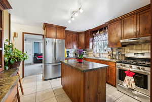 Kitchen featuring stainless steel appliances, light tile patterned flooring, a center island, backsplash, and sink