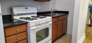 Unit # 3 Kitchen with white appliances, brown cabinetry, dark stone countertops, and light tile patterned floors