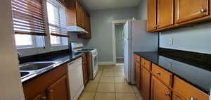 Unit # 9 Kitchen featuring brown cabinets, white appliances, light tile patterned floors, under cabinet range hood, and dark stone counters