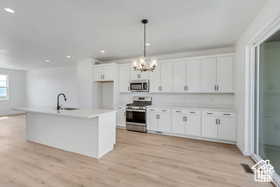 Kitchen with a kitchen island with sink, stainless steel appliances, decorative light fixtures, sink, and white cabinets