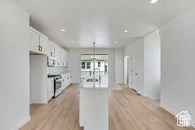 Kitchen with a center island with sink, light wood-type flooring, white cabinetry, stainless steel appliances, and hanging light fixtures
