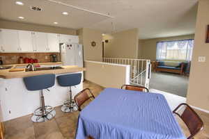 Interior space featuring white refrigerator, sink, tasteful backsplash, white cabinets, and a breakfast bar area