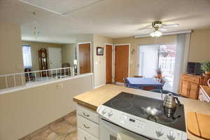 Kitchen featuring a textured ceiling, white cabinets, tile counters, ceiling fan, and electric range oven