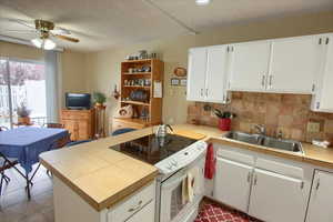 Kitchen featuring white electric range, tile counters, sink, and white cabinetry