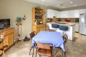 Kitchen featuring white cabinets, white refrigerator, backsplash, and a kitchen island with sink