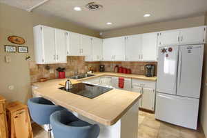 Kitchen with white appliances, sink, white cabinetry, a kitchen bar, and kitchen peninsula