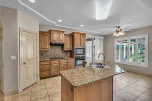 Kitchen with brown cabinetry, under cabinet range hood, black appliances, a sink, and light tile patterned flooring