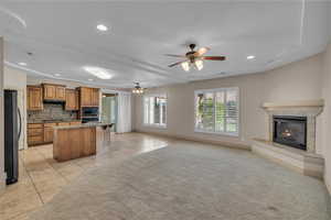 Kitchen featuring a tiled fireplace, black appliances, open floor plan, and brown cabinets