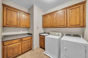 Clothes washing area featuring a sink, baseboards, light tile patterned flooring, washer and clothes dryer, and cabinet space