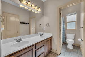 Bathroom with baseboards, toilet, double vanity, and a sink