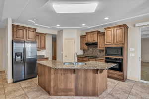 Kitchen with dark stone counters, under cabinet range hood, brown cabinets, black appliances, and a sink