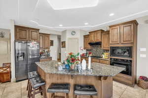 Kitchen with appliances with stainless steel finishes, stone counters, a kitchen breakfast bar, an island with sink, and tasteful backsplash