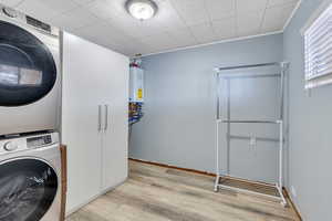 Clothes washing area with light wood-type flooring, stacked washer / dryer, and tankless water heater