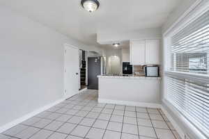 Kitchen with tile countertops, white cabinetry, stainless steel refrigerator, black oven, and kitchen peninsula