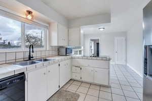 Kitchen with tile countertops, white cabinets, black appliances, light tile patterned flooring, and sink