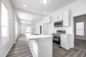 Kitchen featuring hardwood / wood-style floors, appliances with stainless steel finishes, sink, white cabinetry, and an island with sink