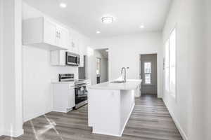 Kitchen featuring appliances with stainless steel finishes, white cabinets, hardwood / wood-style floors, sink, and a kitchen island with sink