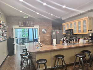 Kitchen with a kitchen bar, appliances with stainless steel finishes, sink, and brick wall