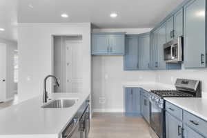 Kitchen featuring appliances with stainless steel finishes, a sink, light wood finished floors, light countertops, and baseboards