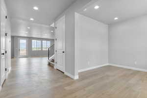 Empty room with stairs, light wood finished floors, recessed lighting, and baseboards