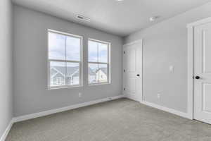 Unfurnished bedroom with carpet flooring, multiple windows, baseboards, and a textured ceiling