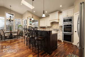 Kitchen with pendant lighting, stainless steel appliances, a center island, light stone countertops, and a kitchen bar