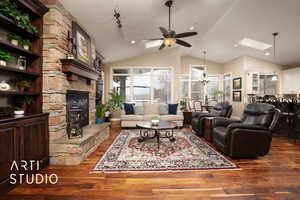 Living room with ceiling fan with notable chandelier, high vaulted ceiling, a fireplace, a skylight, and dark hardwood / wood-style flooring