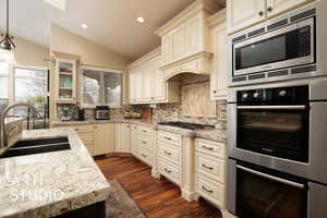 Kitchen featuring lofted ceiling, sink, hanging light fixtures, stainless steel appliances, and cream cabinetry