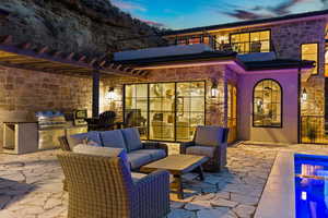 Patio terrace at dusk featuring grilling area, exterior kitchen, an outdoor living space, and a balcony