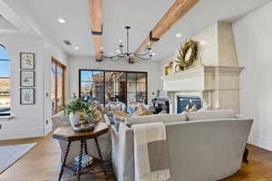 Living room with a fireplace, hardwood / wood-style flooring, a notable chandelier, and beam ceiling