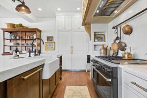 Kitchen featuring light hardwood / wood-style flooring, high end stainless steel range oven, light stone countertops, white cabinets, and wall chimney exhaust hood