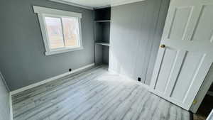 Unfurnished bedroom featuring light wood-type flooring, a closet, and wooden walls