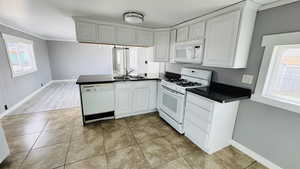 Kitchen featuring sink, white appliances, white cabinetry, and plenty of natural light