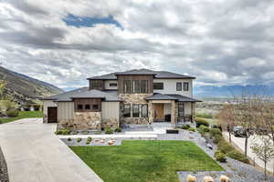 Prairie-style home featuring a porch, driveway, a garage, a front lawn, and stone siding