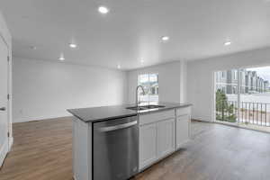 Kitchen with an island with sink, hardwood / wood-style flooring, sink, dishwasher, and white cabinets