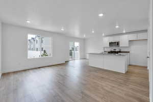 Kitchen with white cabinets, a center island with sink, stainless steel appliances, and light wood-type flooring