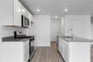 Kitchen with light wood-type flooring, a center island with sink, sink, appliances with stainless steel finishes, and white cabinets