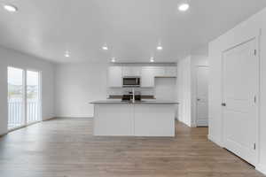 Kitchen featuring appliances with stainless steel finishes, light wood-type flooring, white cabinets, sink, and a kitchen island with sink