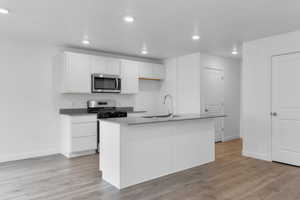 Kitchen with white cabinets, appliances with stainless steel finishes, sink, and a kitchen island with sink