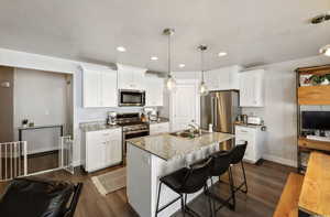 Kitchen with white cabinetry, appliances with stainless steel finishes, sink, and stone countertops