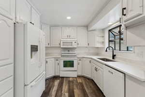 Kitchen with white appliances, white cabinetry, sink, and dark hardwood / wood-style flooring