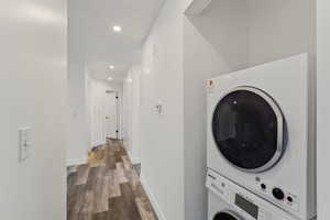 Laundry room featuring stacked washer and dryer and dark hardwood / wood-style flooring