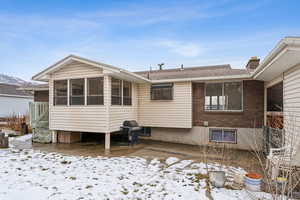 Snow covered rear of property featuring a sunroom