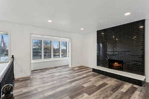 Unfurnished living room with hardwood / wood-style floors, a textured ceiling, and a brick fireplace