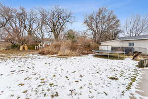 Yard layered in snow with a playground and a trampoline