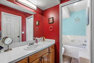 Bathroom featuring toilet, a textured ceiling, vanity, and tiled tub