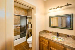 Guest full bathroom with a country flair custom vanity, toilet, tile flooring, and bath / shower combo with privacy door.